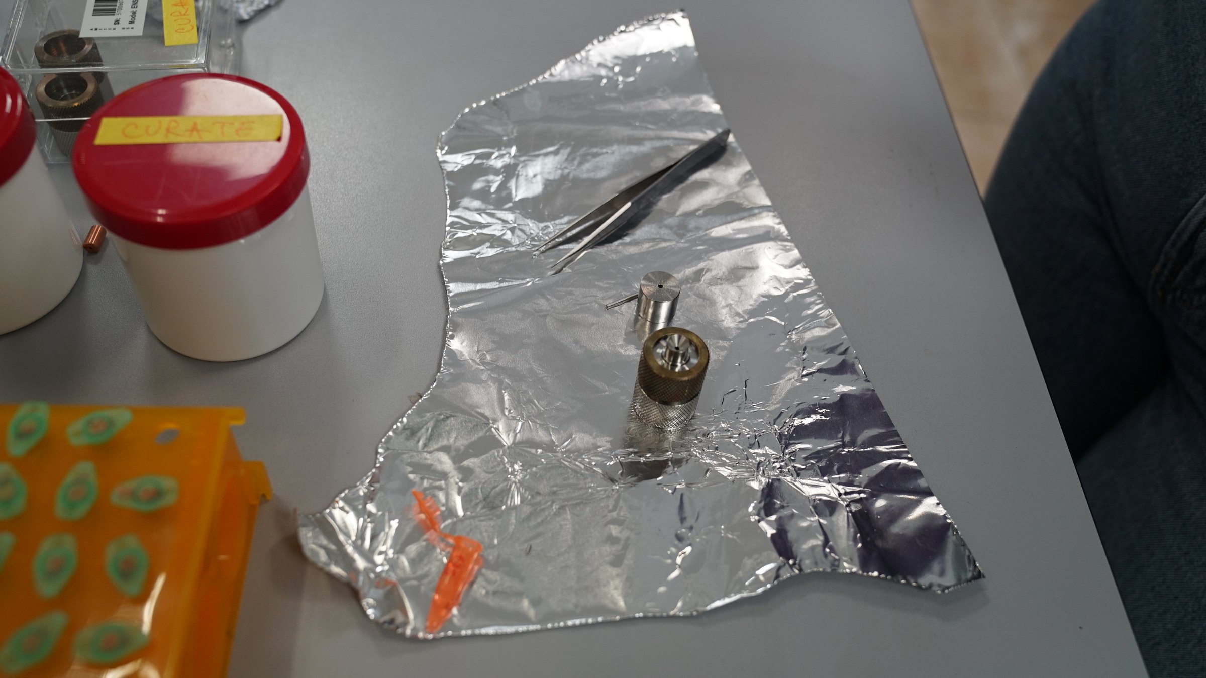 Prepared AMS cathodes — small metal target holders pressed with sample material, on aluminium foil with tweezers, ready to be loaded into the ion source