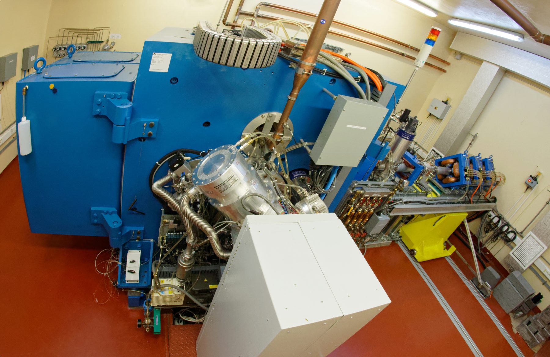 Aerial view of the TR-19 cyclotron — the large blue magnet vault, copper RF line and extraction beamline in the production vault