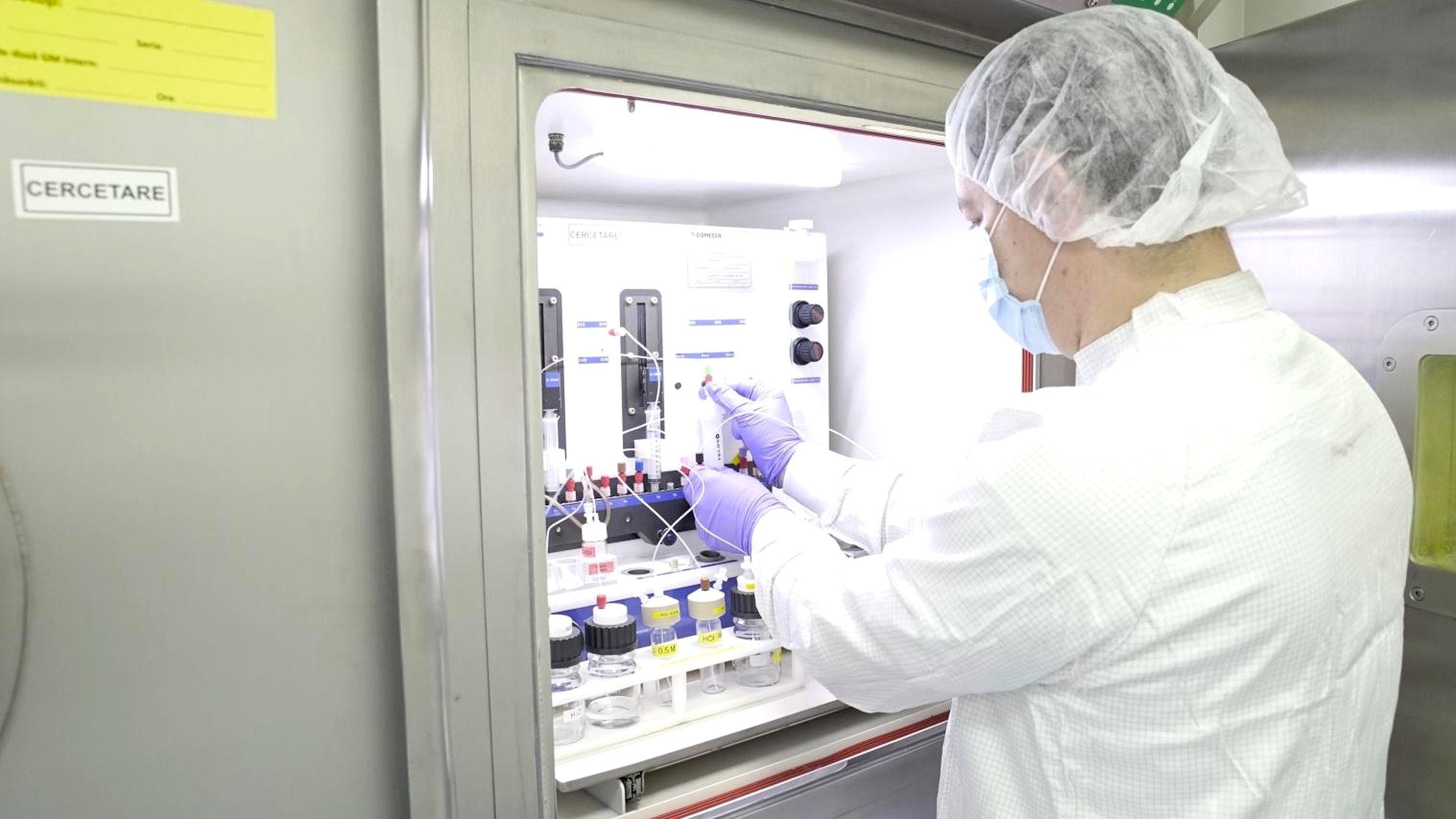 An operator in cleanroom attire working at a COMECER research hot cell, processing an irradiated target through dissolution and radiochemical separation