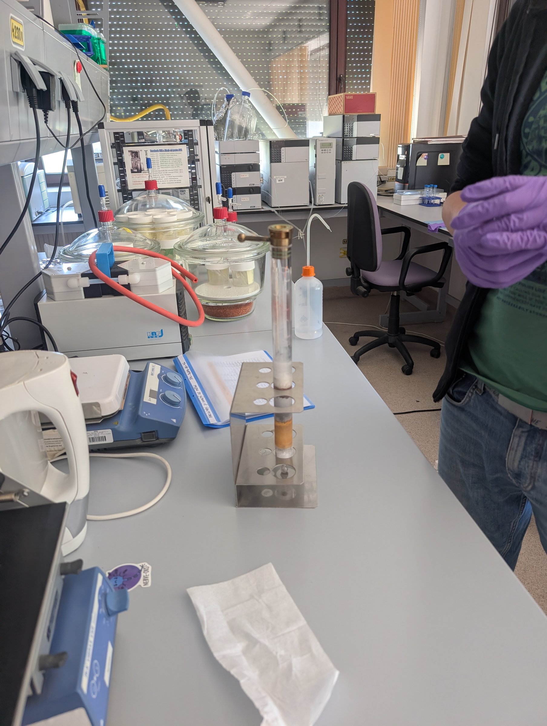 A glass column from the graphitisation line mounted in a stand, with desiccators and reagents on the bench behind