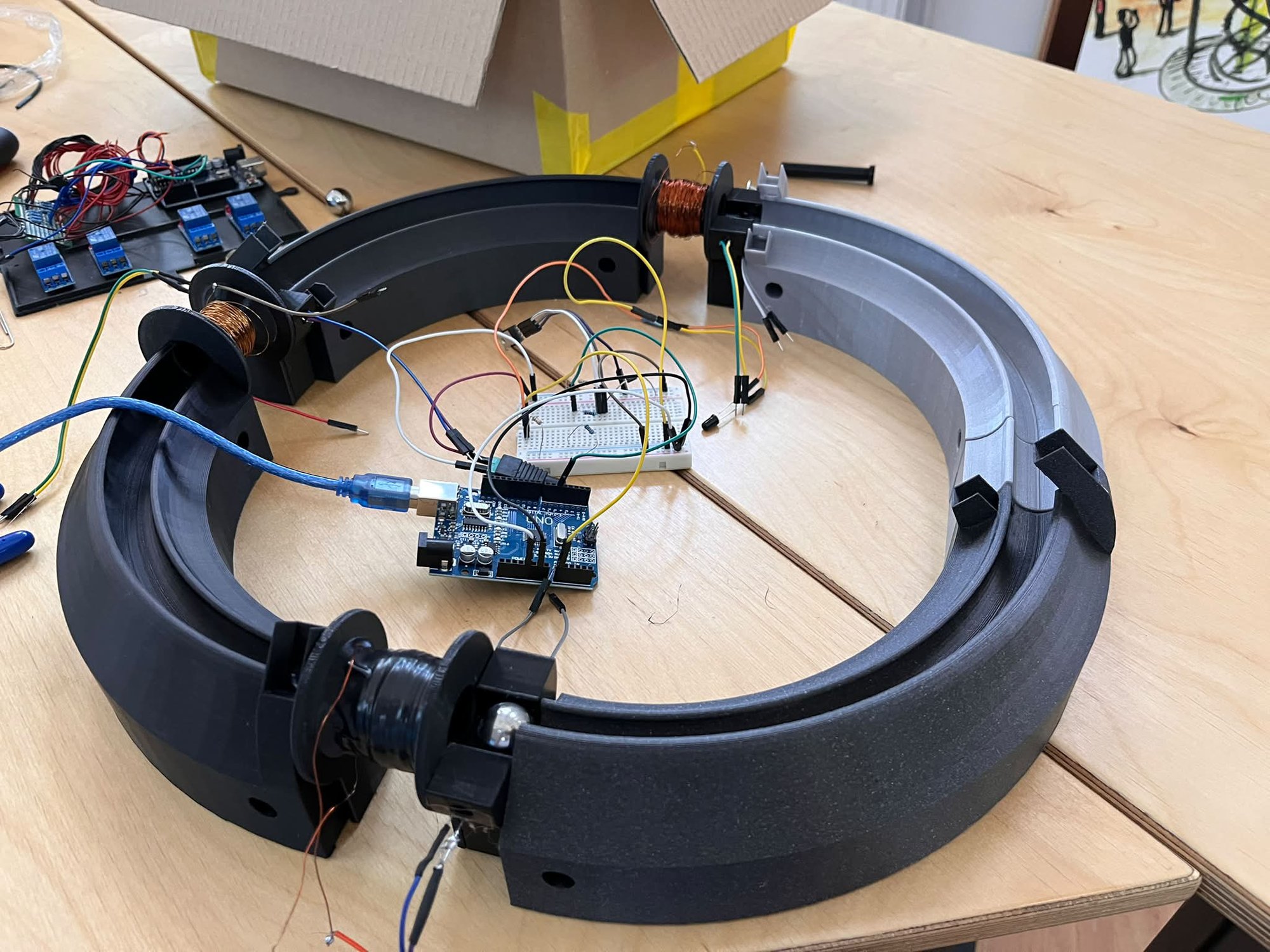 The assembled three-stage electromagnetic accelerator model: a circular 3D-printed track carrying three coils, driven by an Arduino Uno and a breadboard