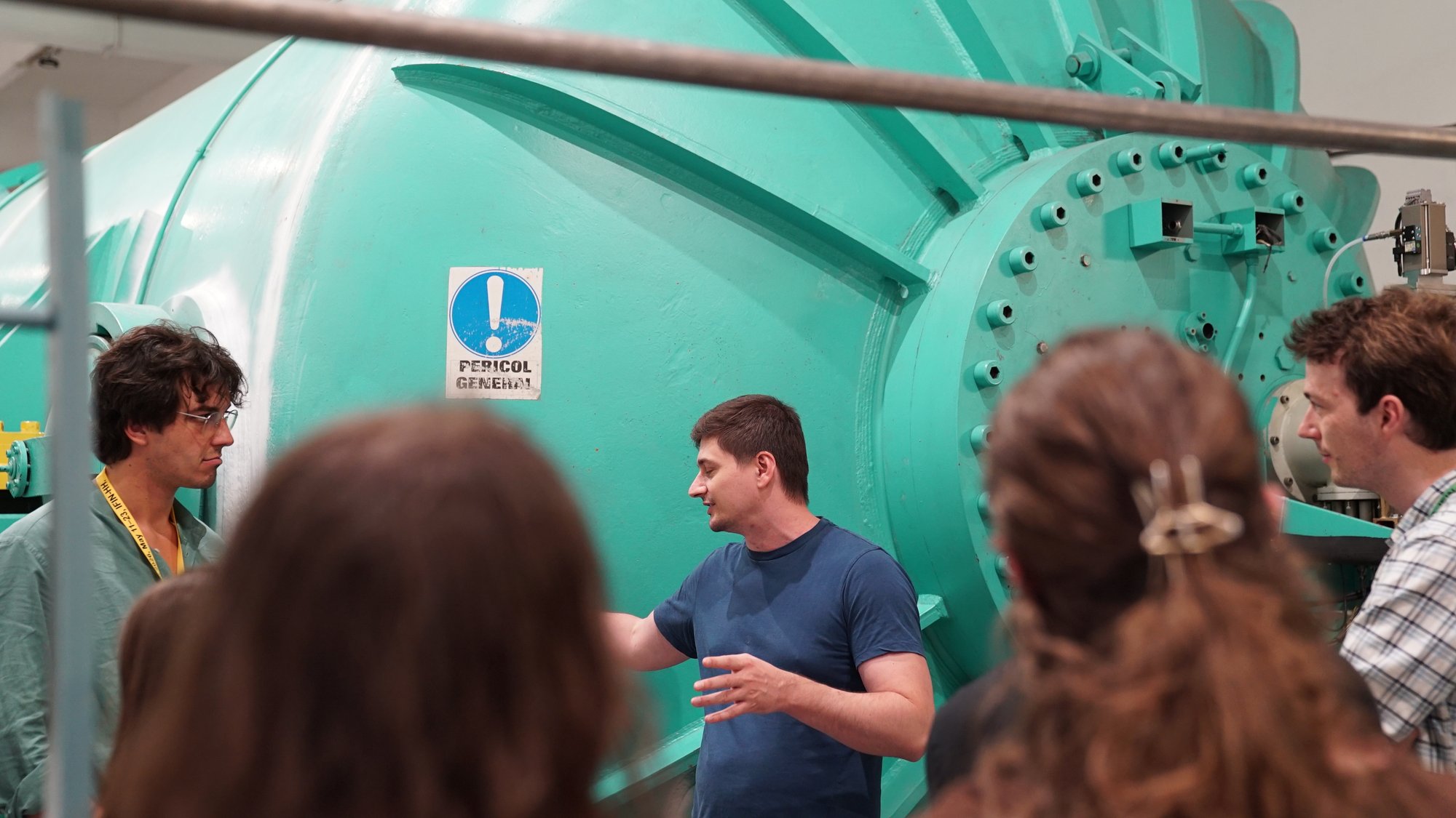 A trainer explains the tandem accelerator's pressure tank to a group of BTS26 trainees gathered around it