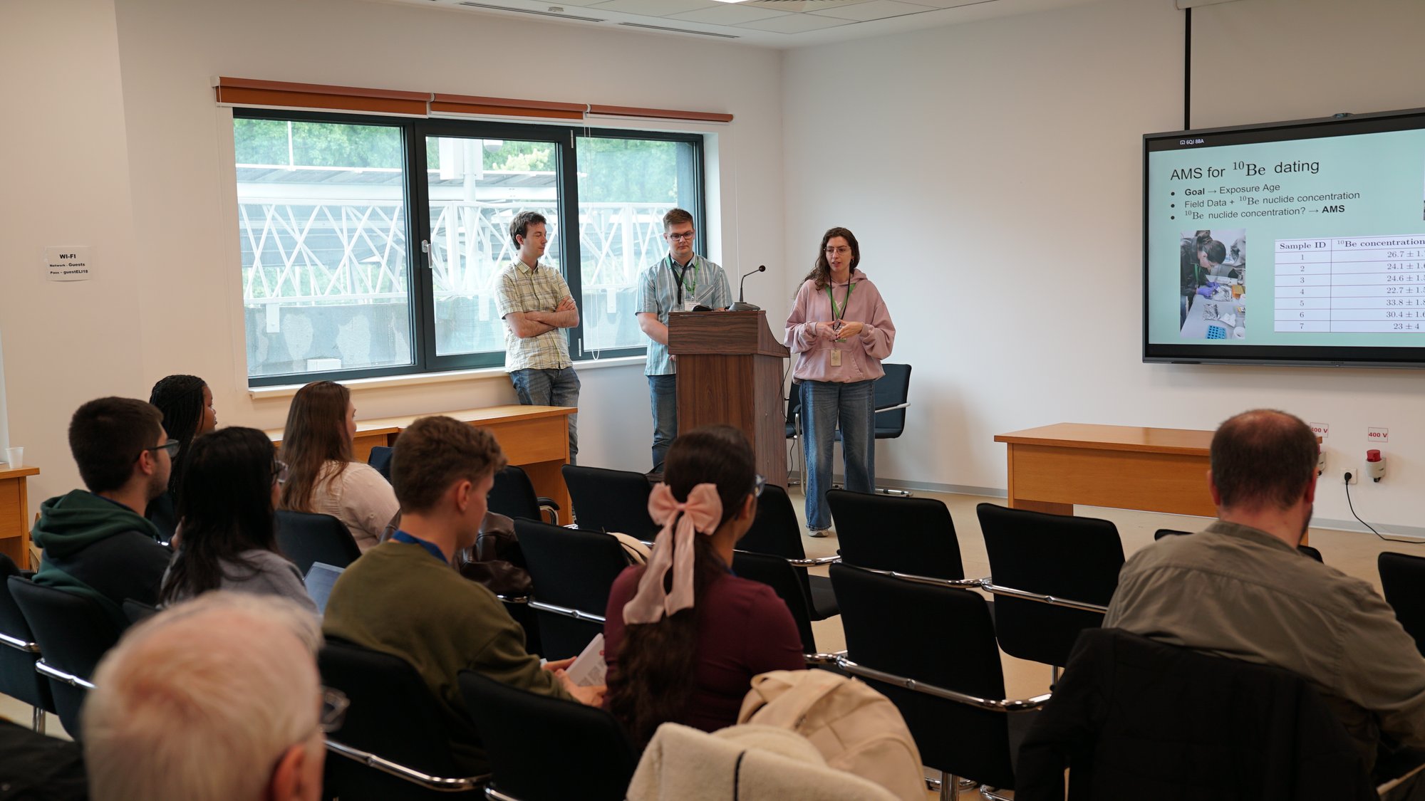 A trainee presenting at the podium, with slides and audience visible