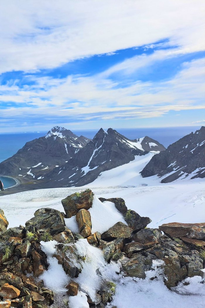 Snow-covered mountain peaks and glaciers on Livingston Island, seen across a rocky foreground