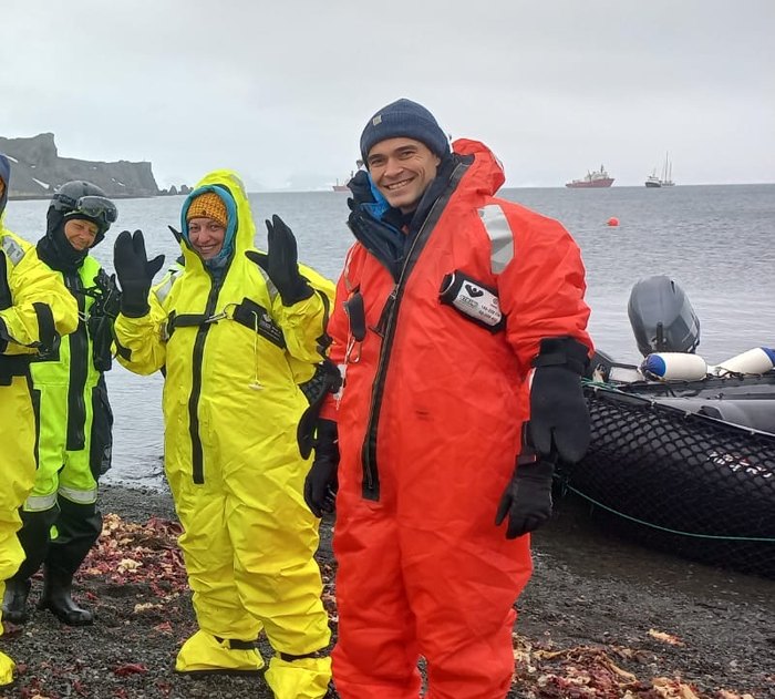 Expedition members in survival suits beside an inflatable boat on the shore