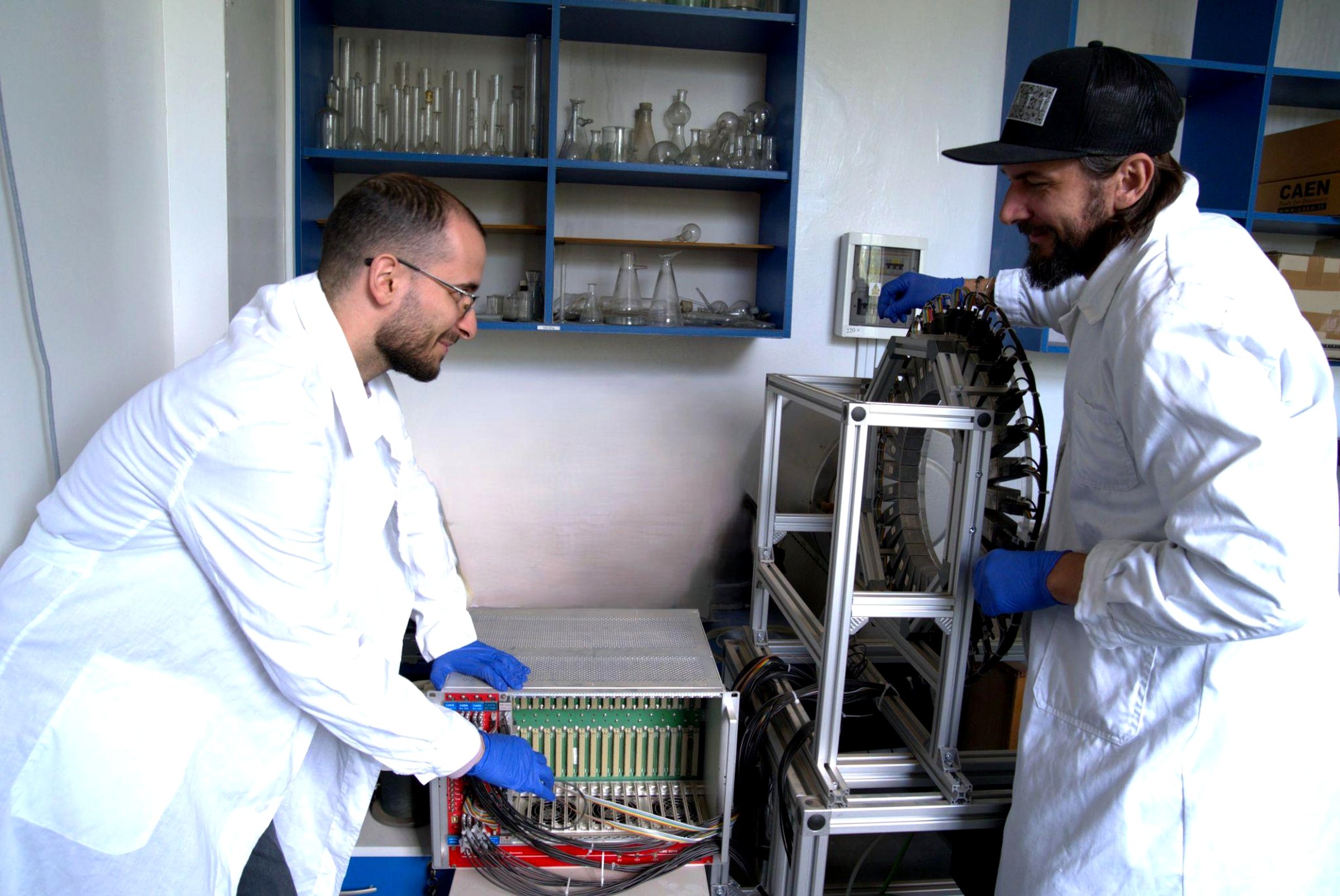 Two DFNA researchers in lab coats assembling micro-PET equipment, handling its ring of detector modules and readout electronics